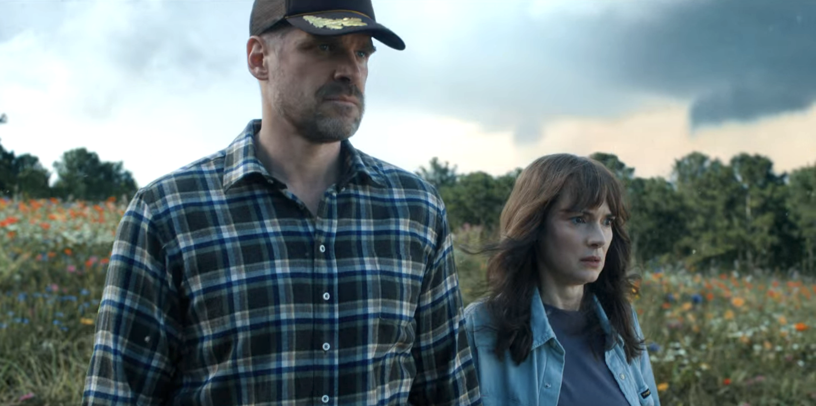 Hopper in a cap and plaid shirt and Joyce standing in a field with flowers