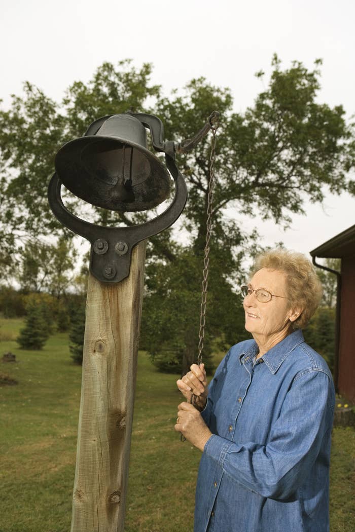 Older woman ringing a large bell outdoors