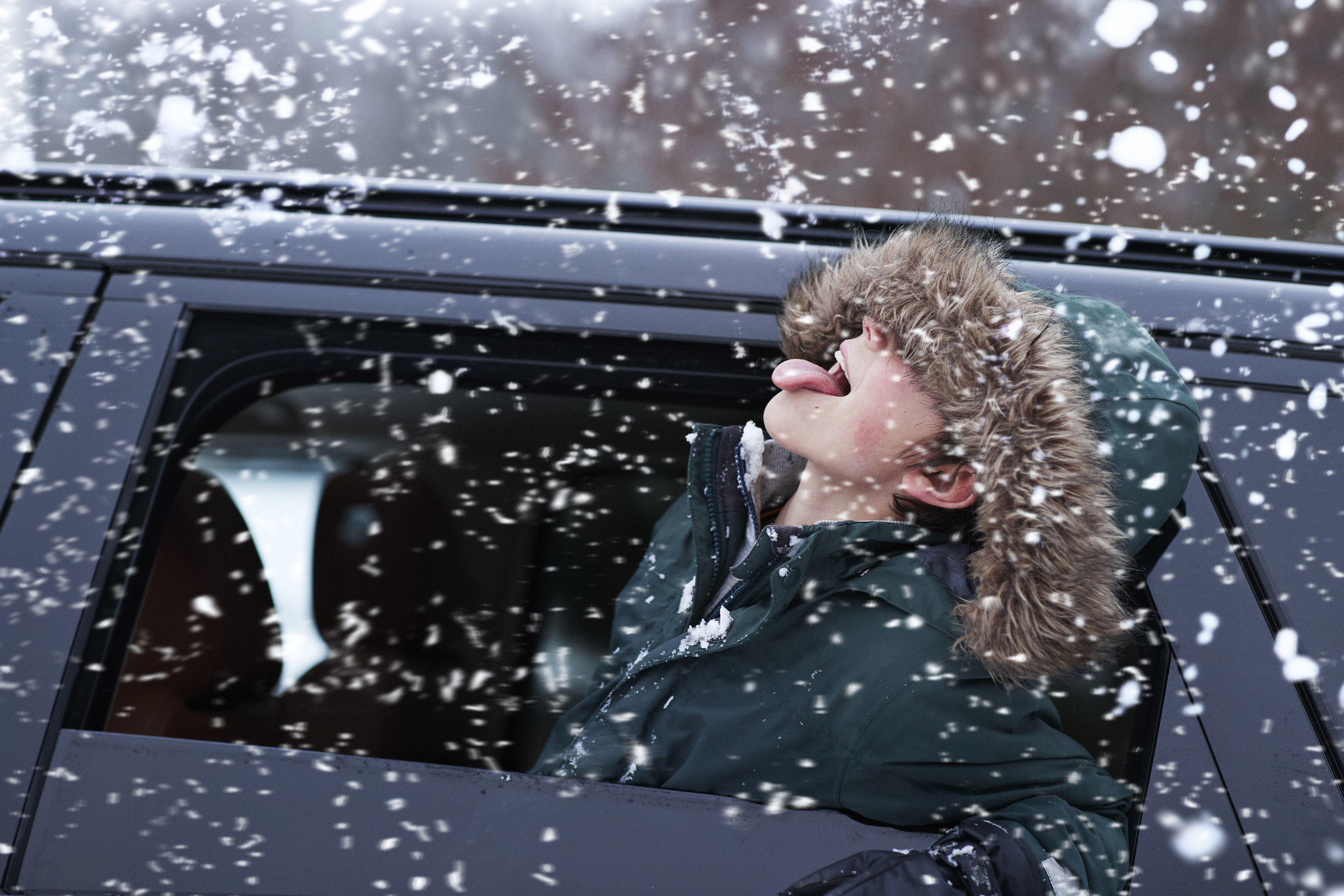 Person sticking their head out of a car window with their tongue out to taste snow