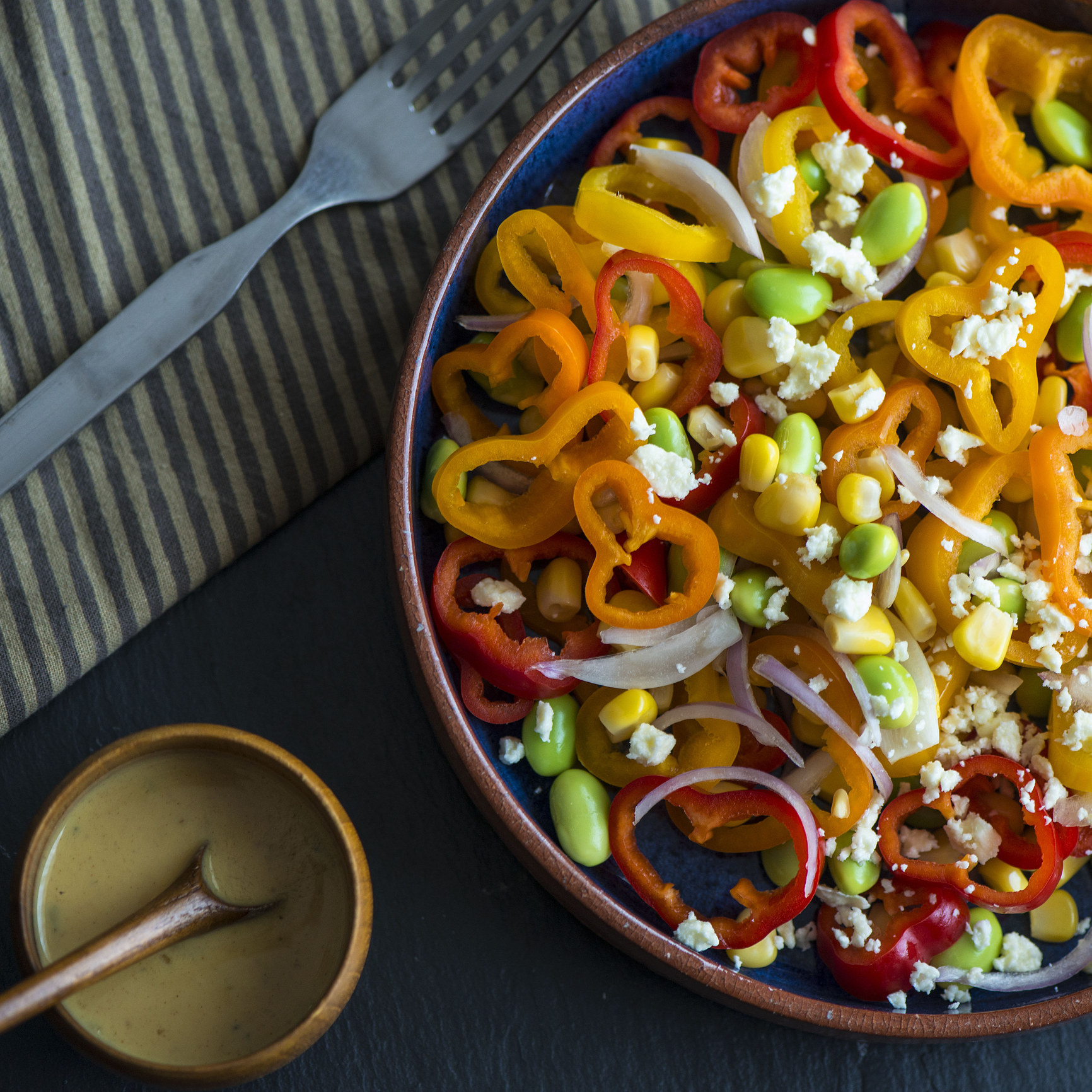 A bowl of salad topped with peppers, edamame, corn, and cheese.