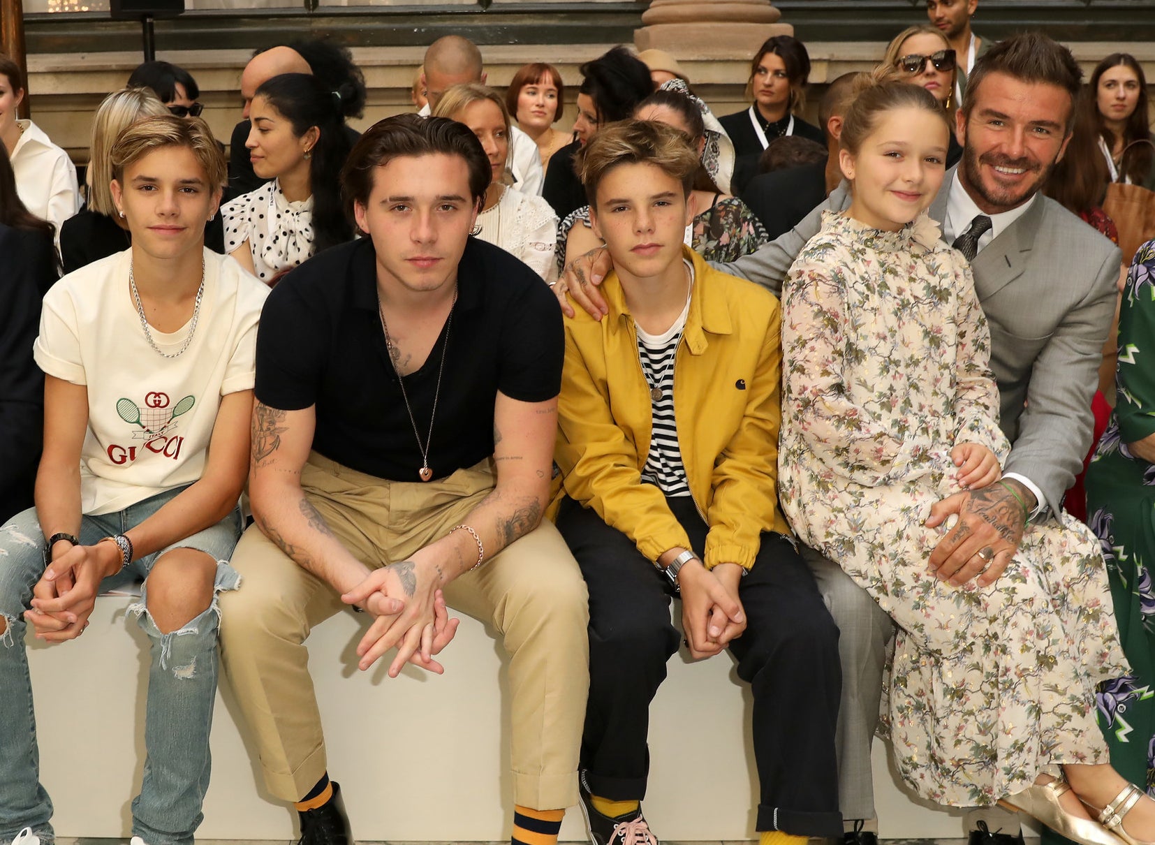 Harper sits on her dad&#x27;s lap at a fashion show while sitting next to her brothers