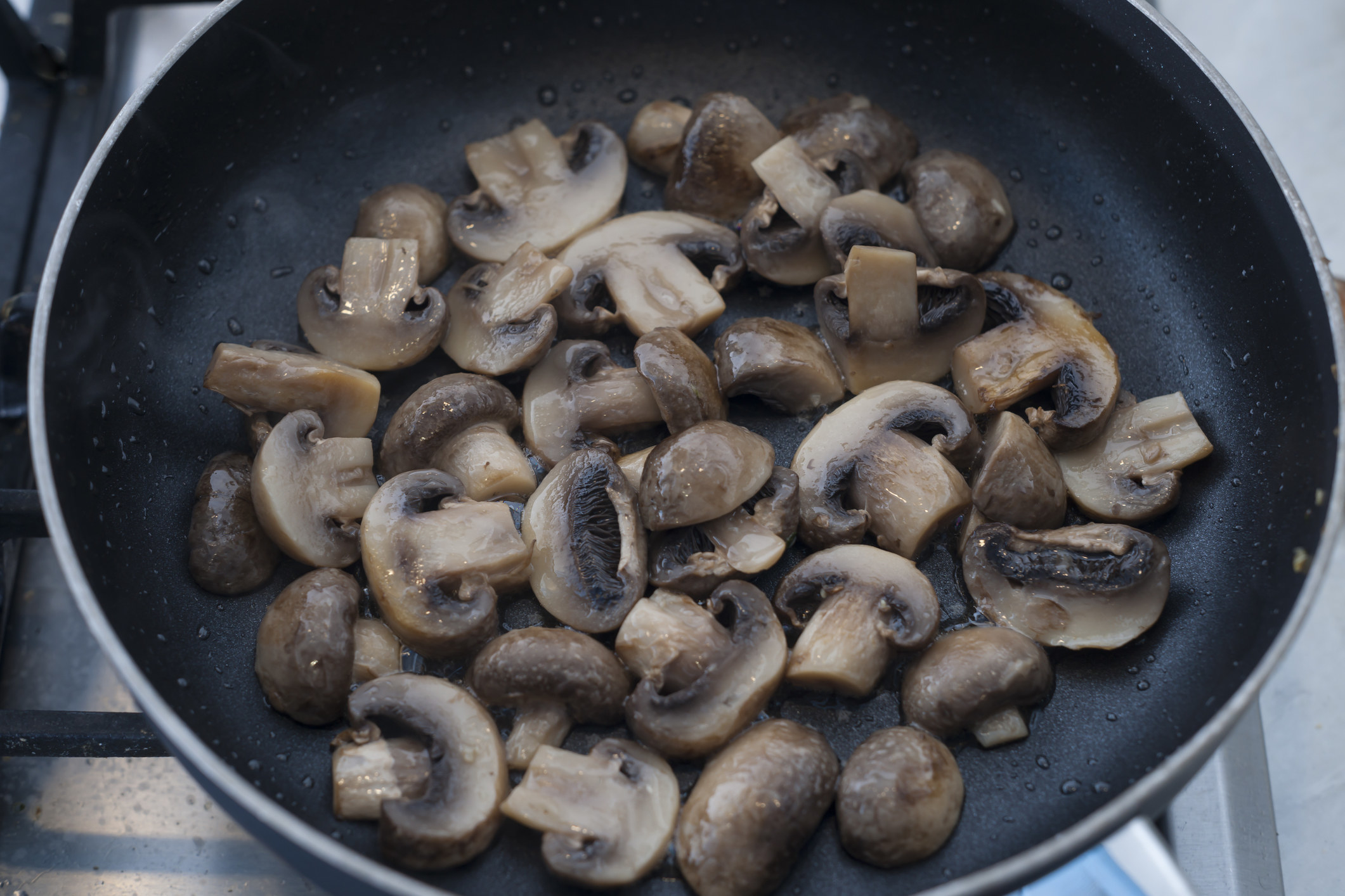 Sliced button mushrooms in a skillet.