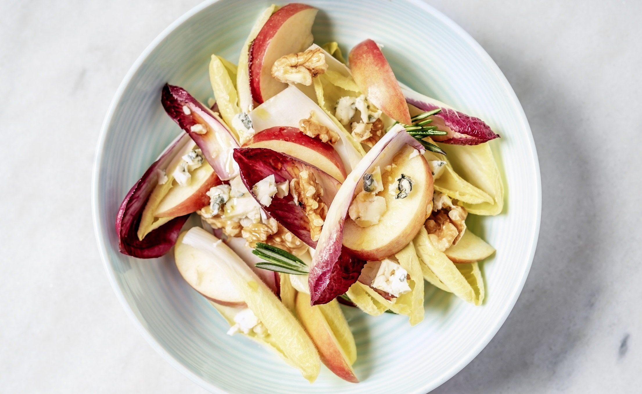 A bowl of endive salad with slices of apple, walnuts, and blue cheese.