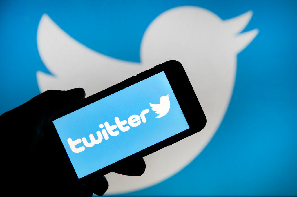 Person holding a phone showing the Twitter logo