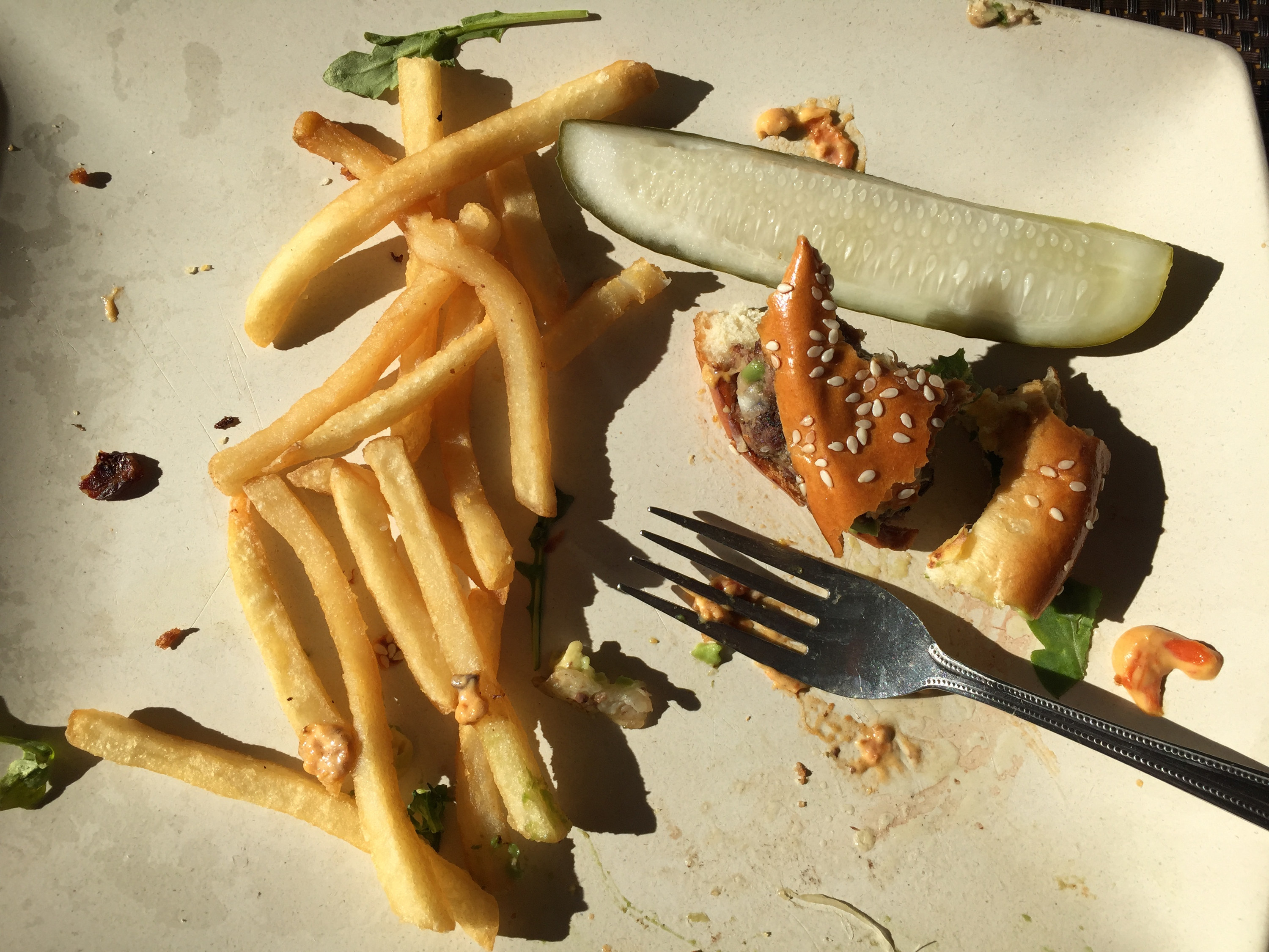 Remains of a meals of hamburger, french fries and pickle with fork.