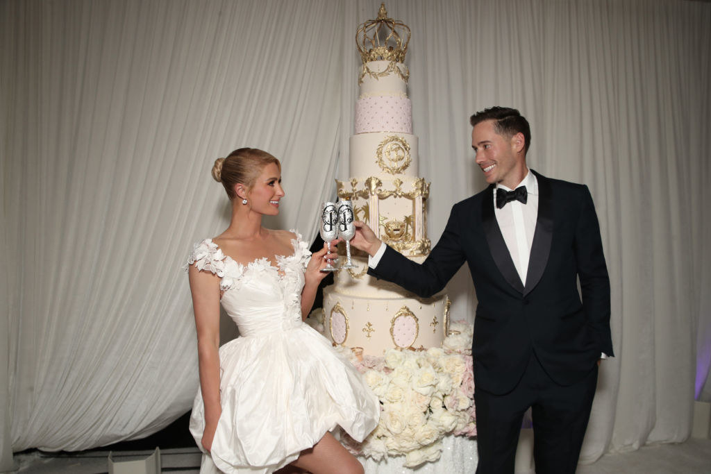 Paris and her husband toasting each other in front of the wedding cake