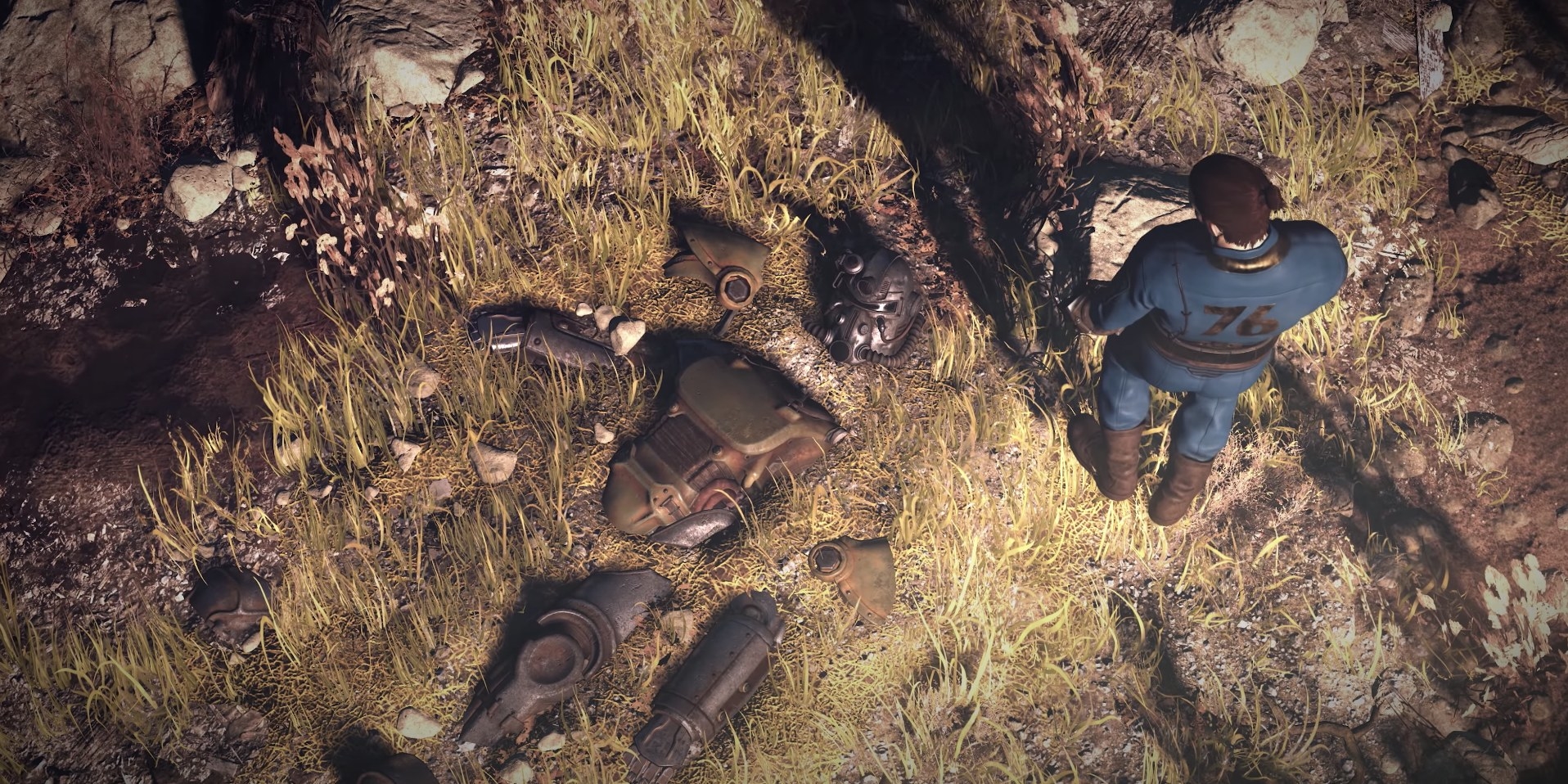A man in a blue jumpsuit examines a decaying suit of futuristic armor in the ground.