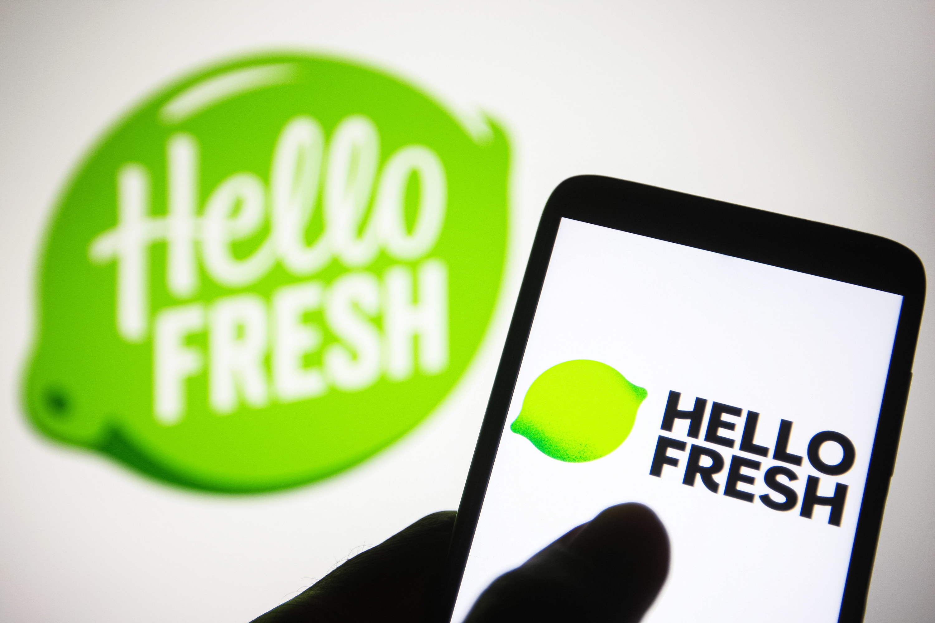 Someone using the HelloFresh app on their phone, near a wall with the HelloFresh logo on it