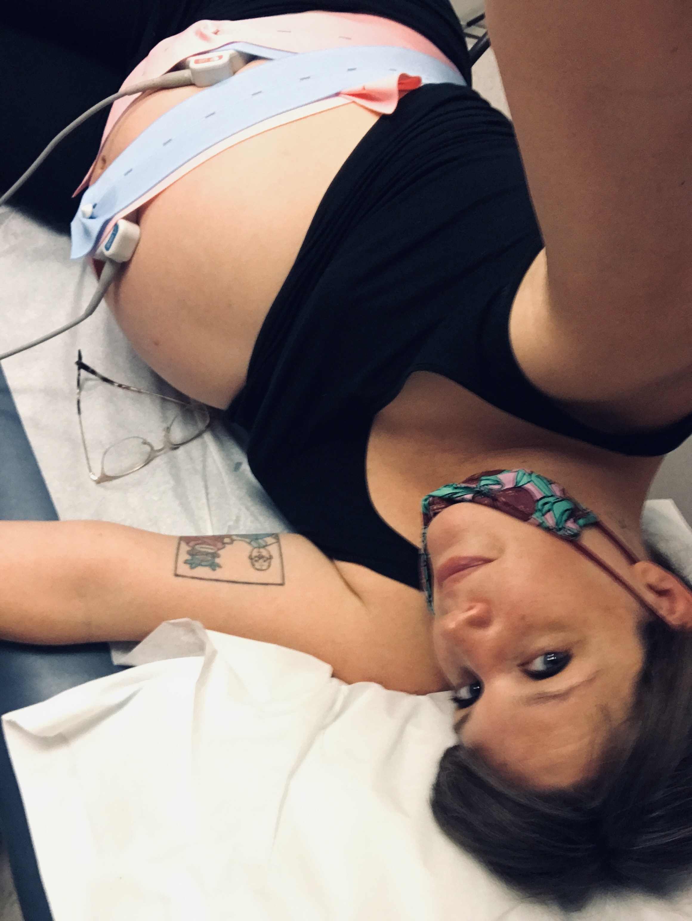 Sophie laying on an exam table at the doctors office with a heart rate monitor strapped around her pregnant belly.