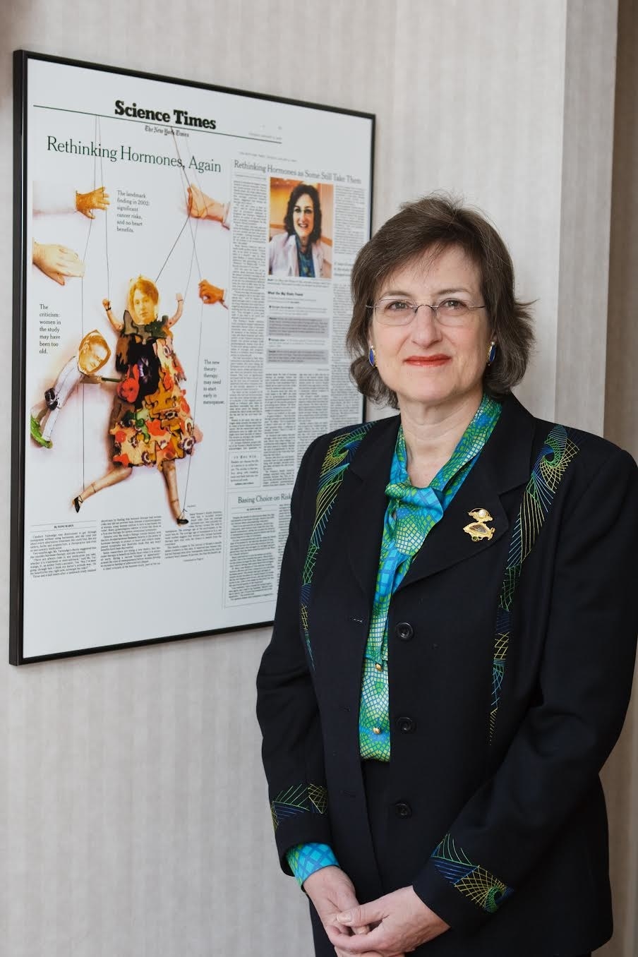 Mary Jane Minkin standing in front of a framed New York Times article on a wall featuring her