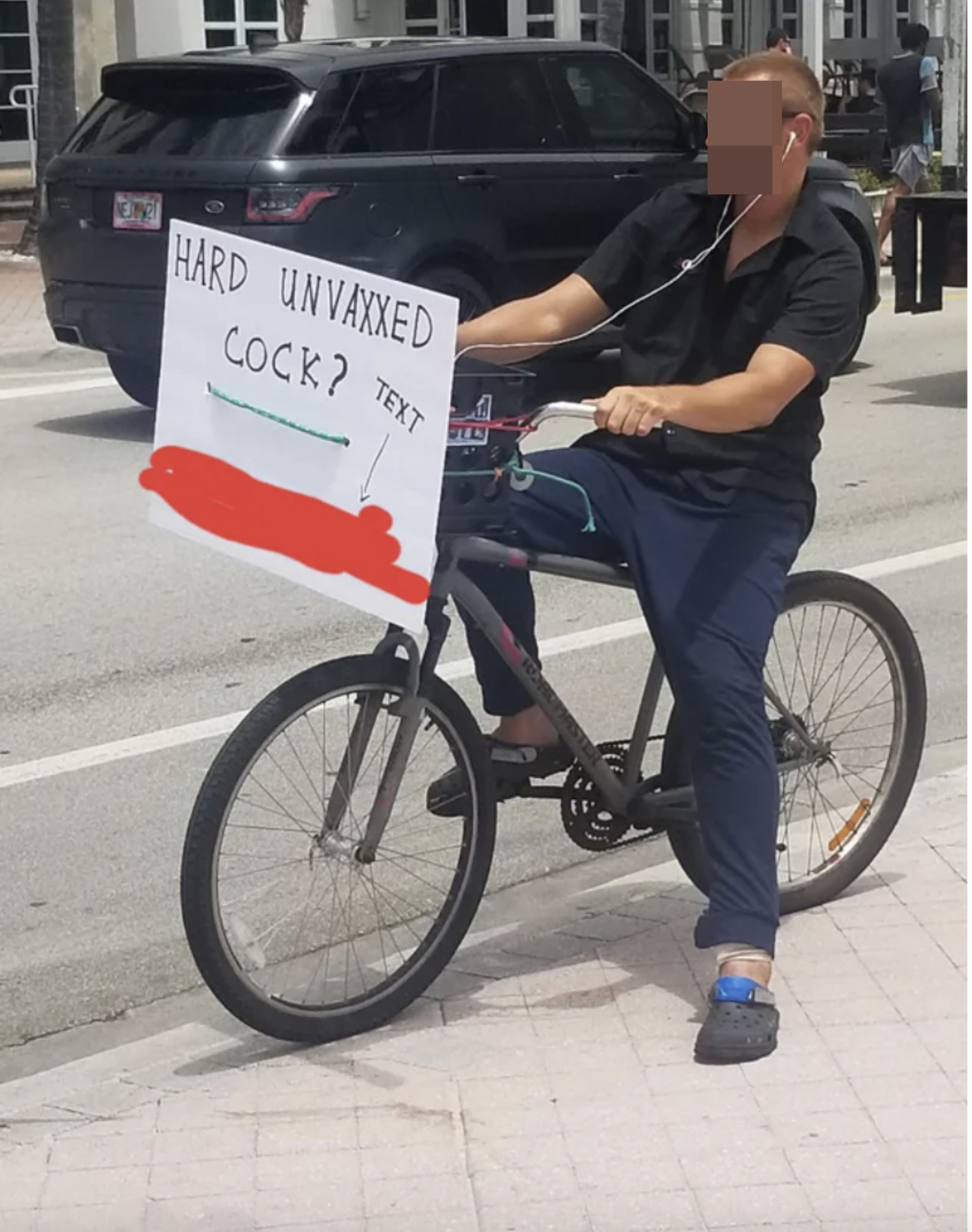 a man riding a bike with a sign that says, &quot;Hard unvaxxed cock — text,&quot; and a phone number