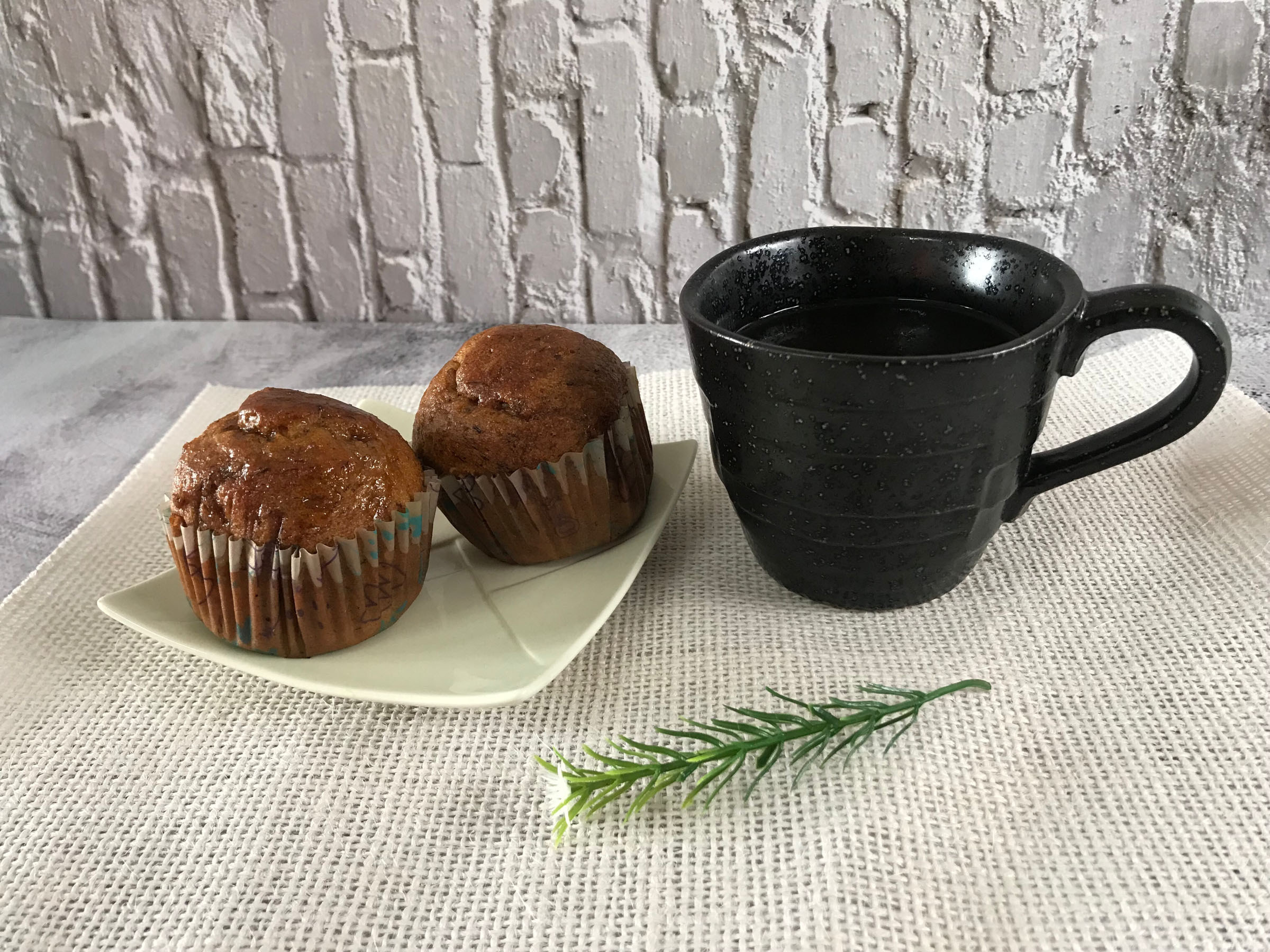 Two muffins on a plate next to a mug