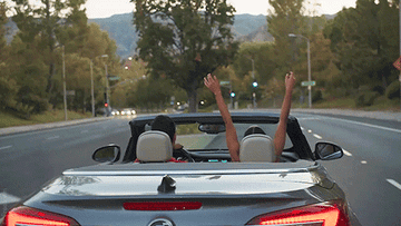 A car driving away with the girl in the passenger seat with her arms up