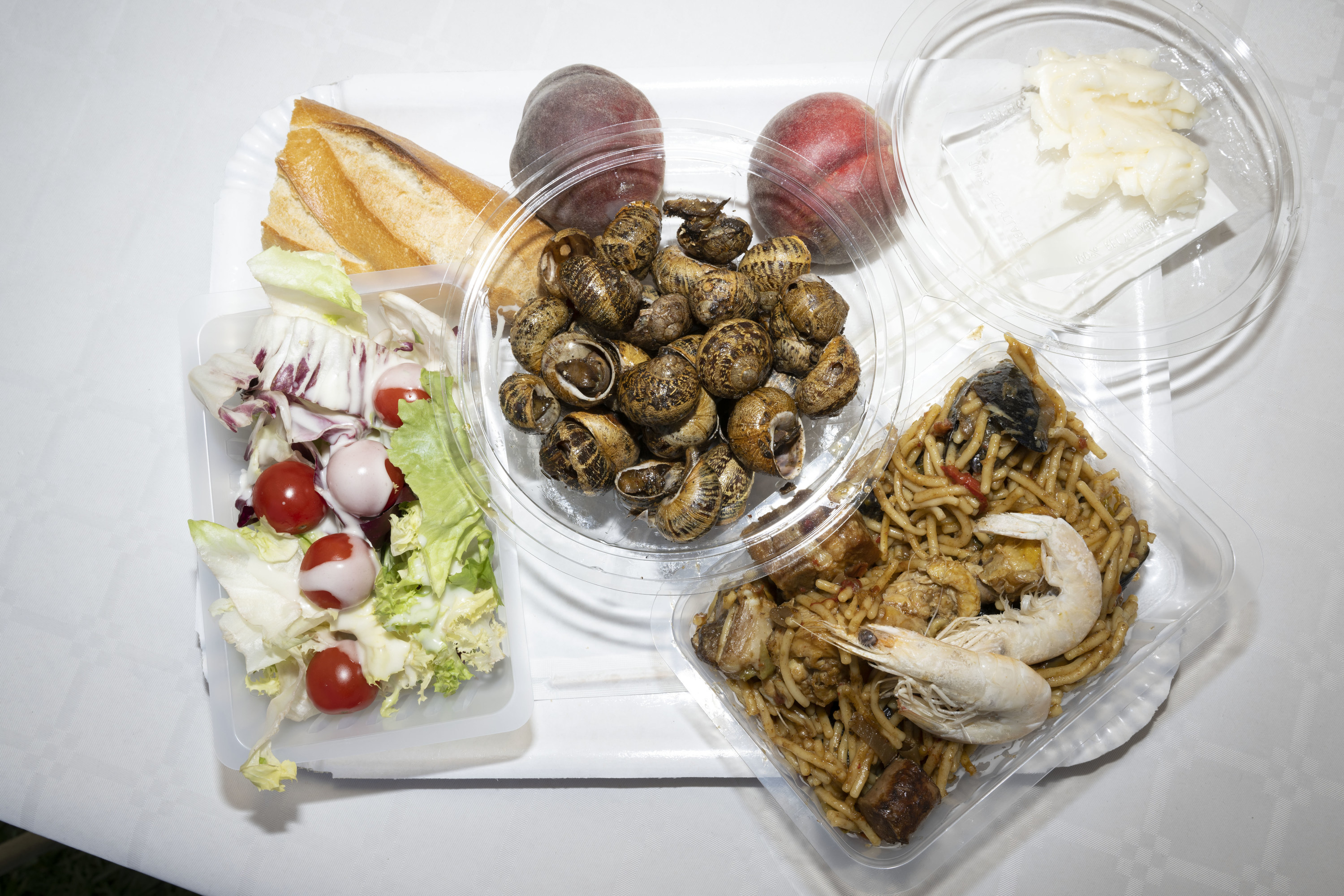 A tray with various plates holding a salad, escargot, paella, peaches, a baguette, and butter