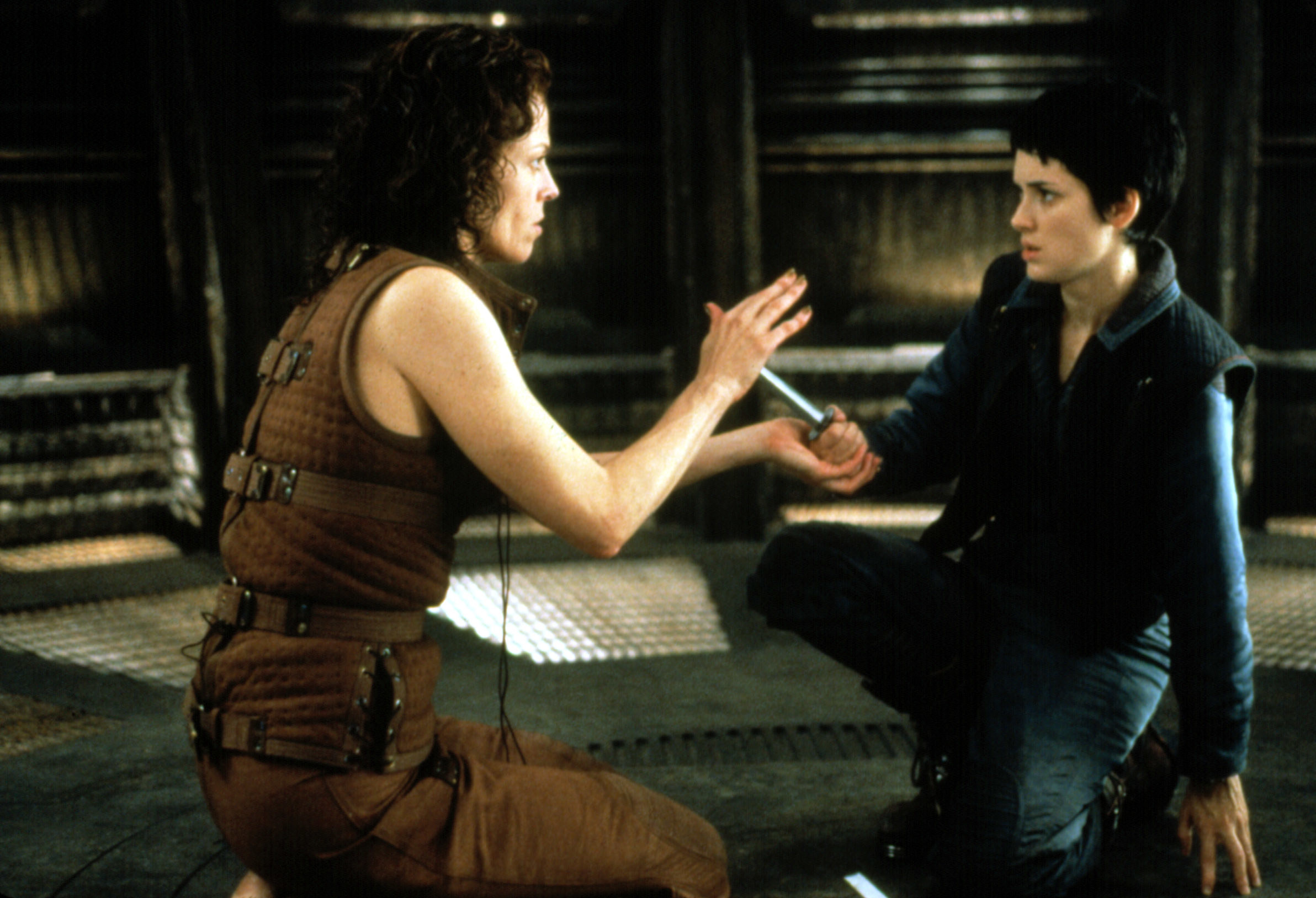 Winona Ryder pointing a weapon at Sigourney Weaver, who holds her hand up to diffuse the situation