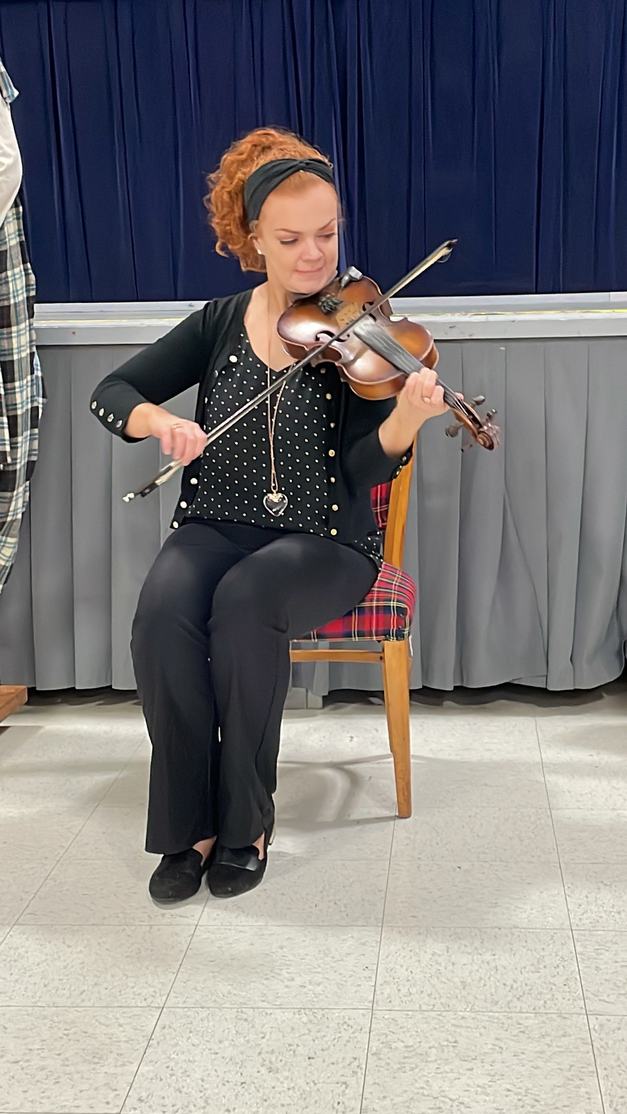 A woman plays the fiddle seated