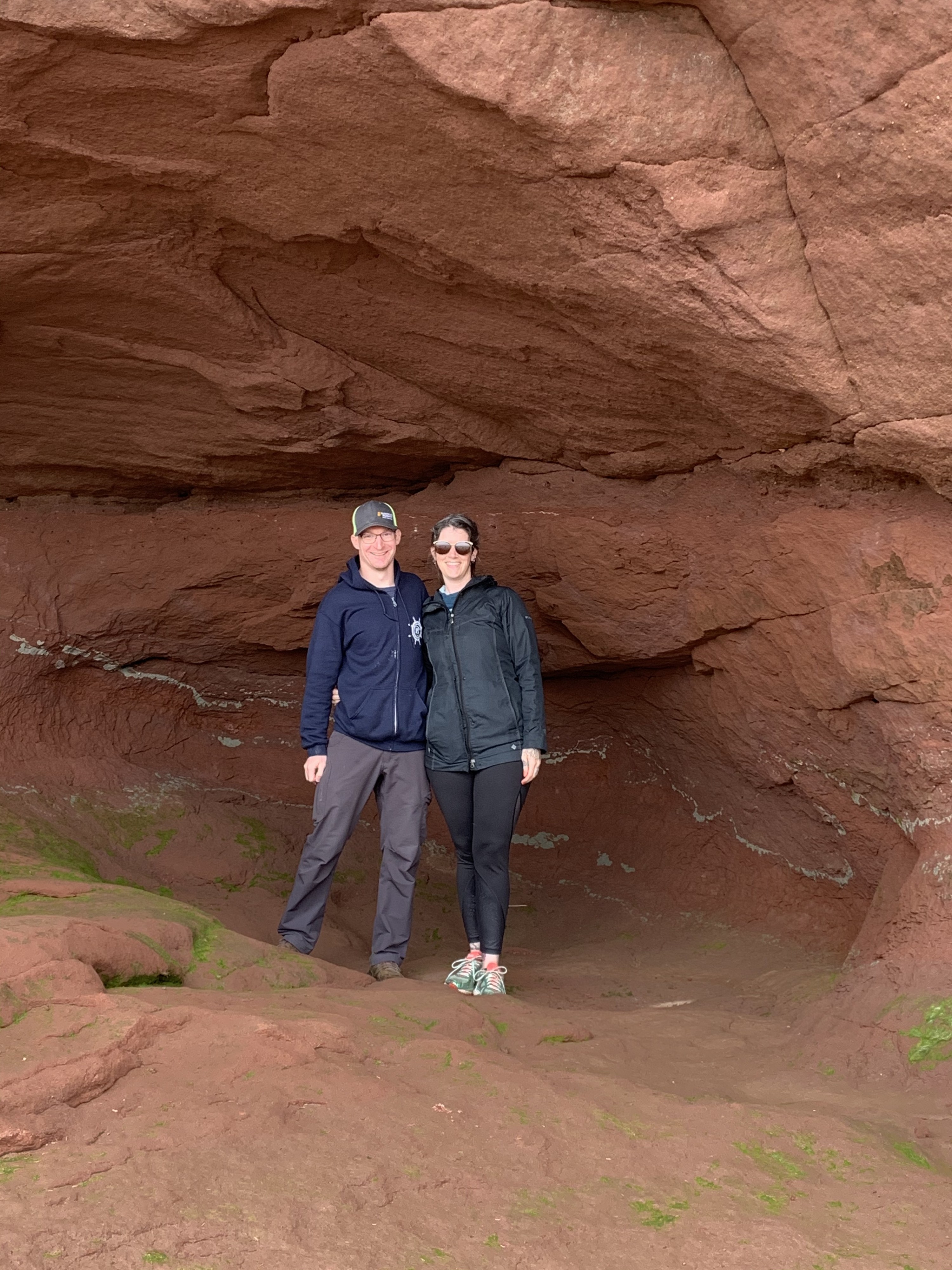 A man and woman stand together in a brown rock alcove along the ocean floor
