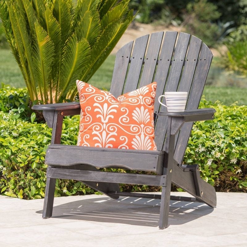 a gray Adirondack chair with an orange pillow and mug on its arm