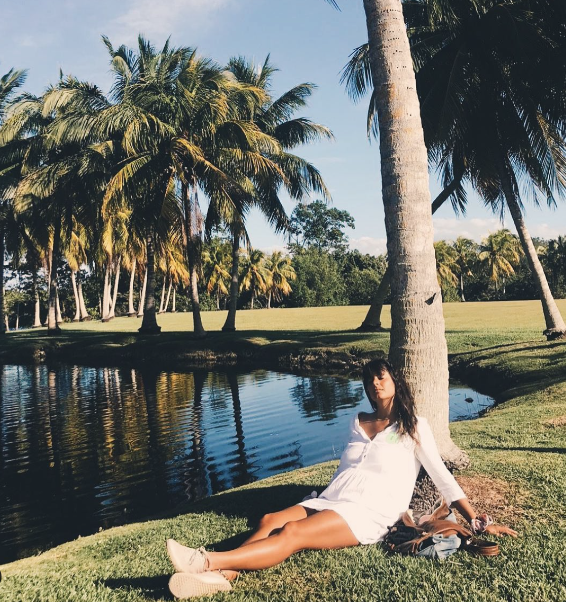Arielle sitting against a palm three by the water