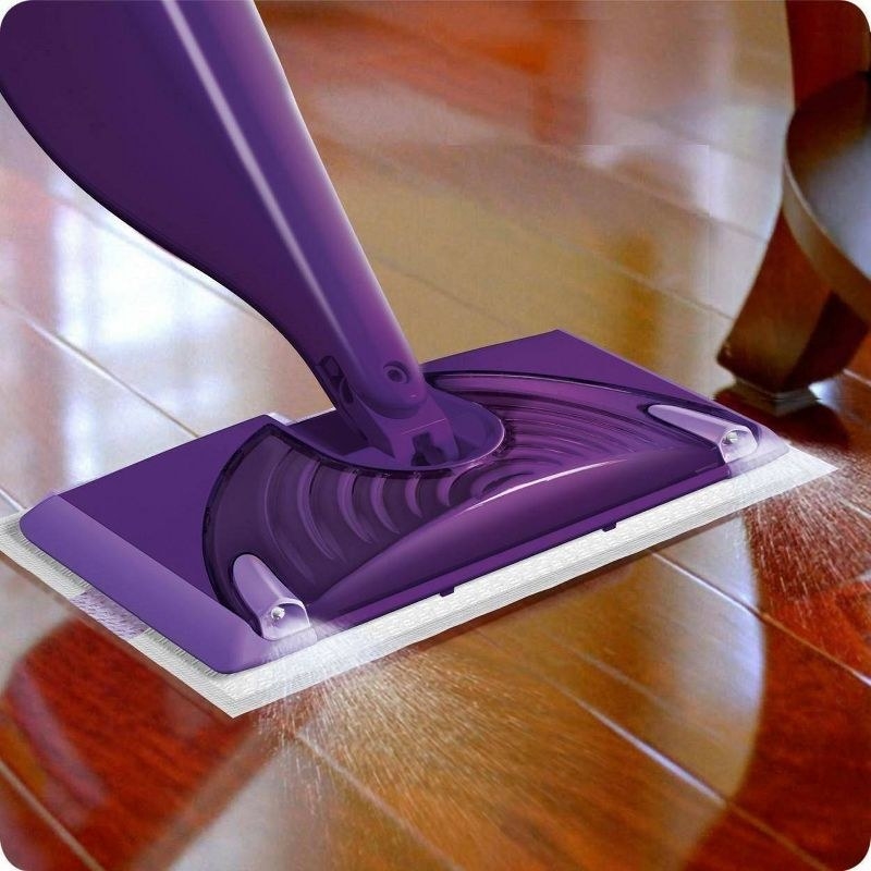 a purple Swiffer WetJet floor mop spraying cleaning solution on a wood floor