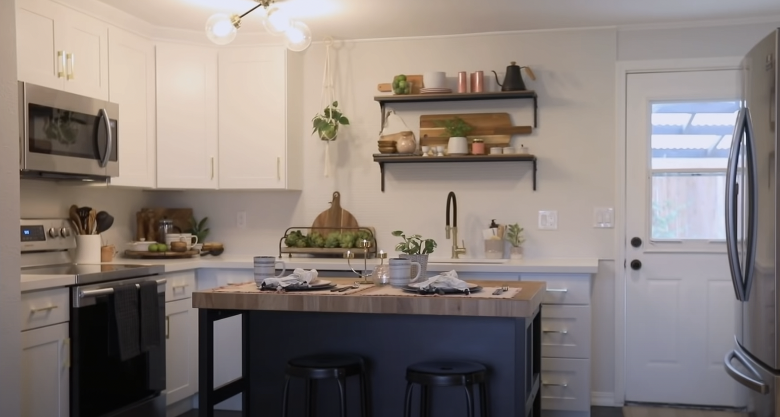 A kitchen designed by Lyndsay and Leslie, including white cabinets and a navy blue island with butcher block countertops
