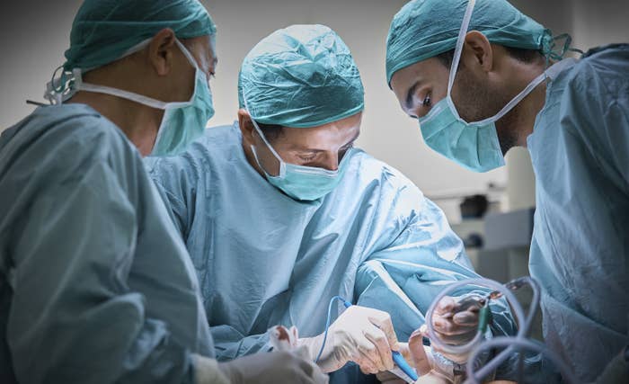 A group of doctors operate on a patient during a breast implant surgery