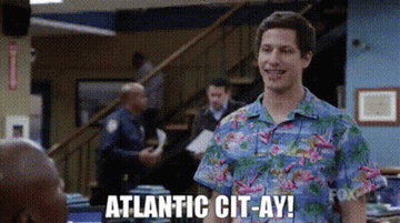Jake stands in a brightly patterned Hawaiian shirt with blue, pink, and green in it as white text appears below him reading &quot;Atlantic Cit-ay!&quot; 