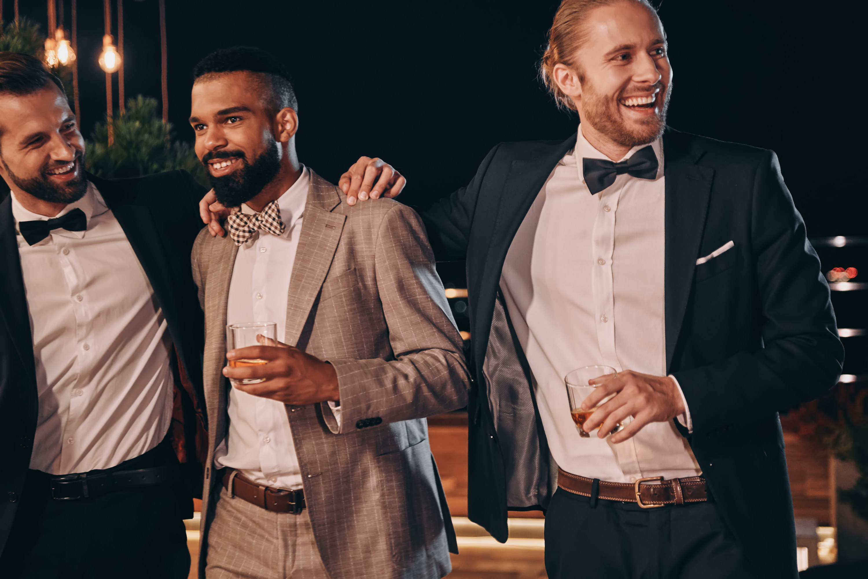 Three men hold drinks in hands, smiling at a wedding