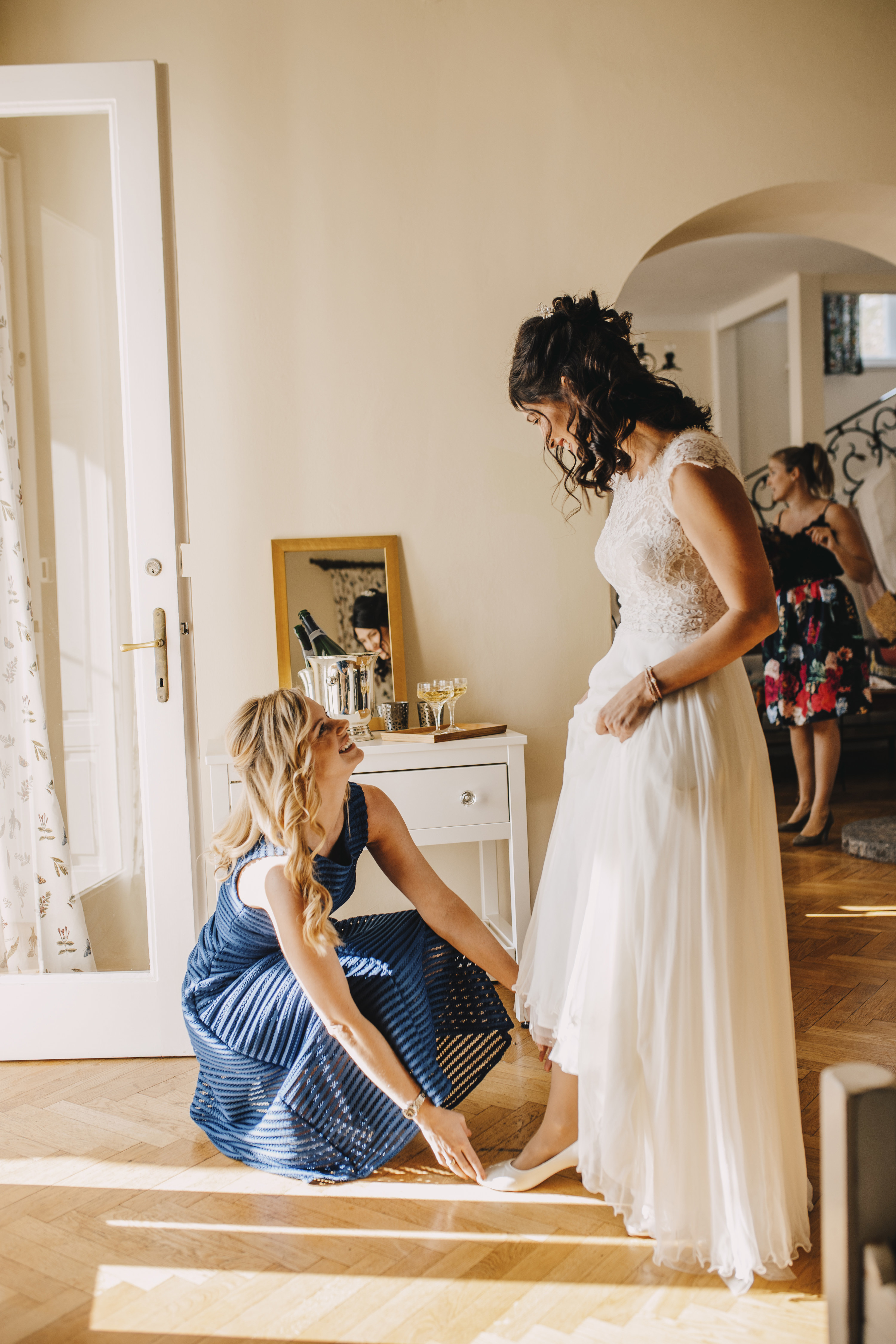 Maid of honor kneeling down and smiling at bride. She helps the bride with her shoe