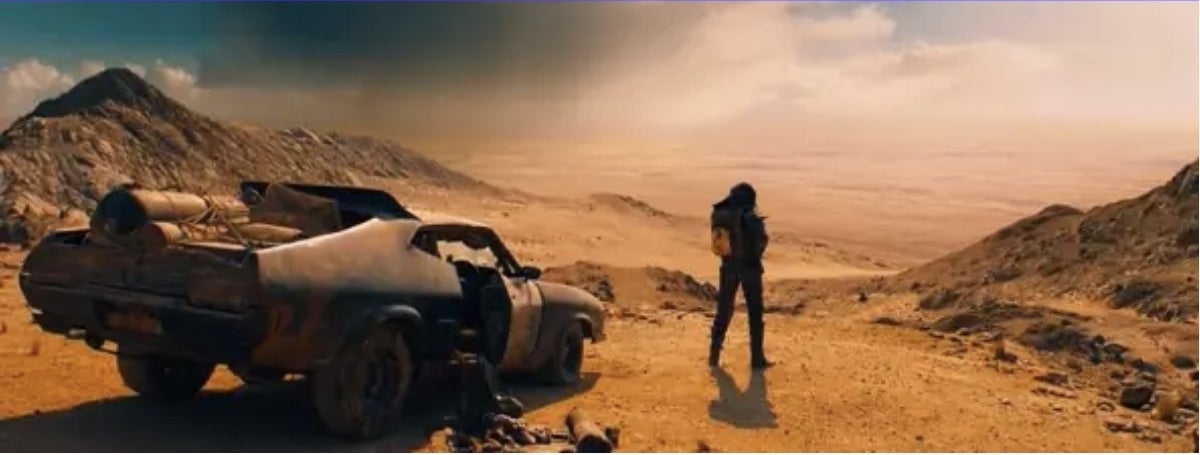 A person standing in front of a burned-out car and looking out over a barren landscape