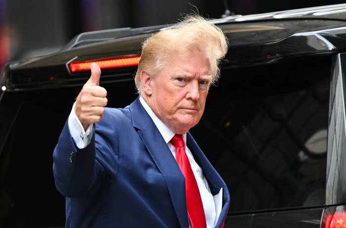 Trump gives a thumbs up as wind blows his hair as he steps into a car