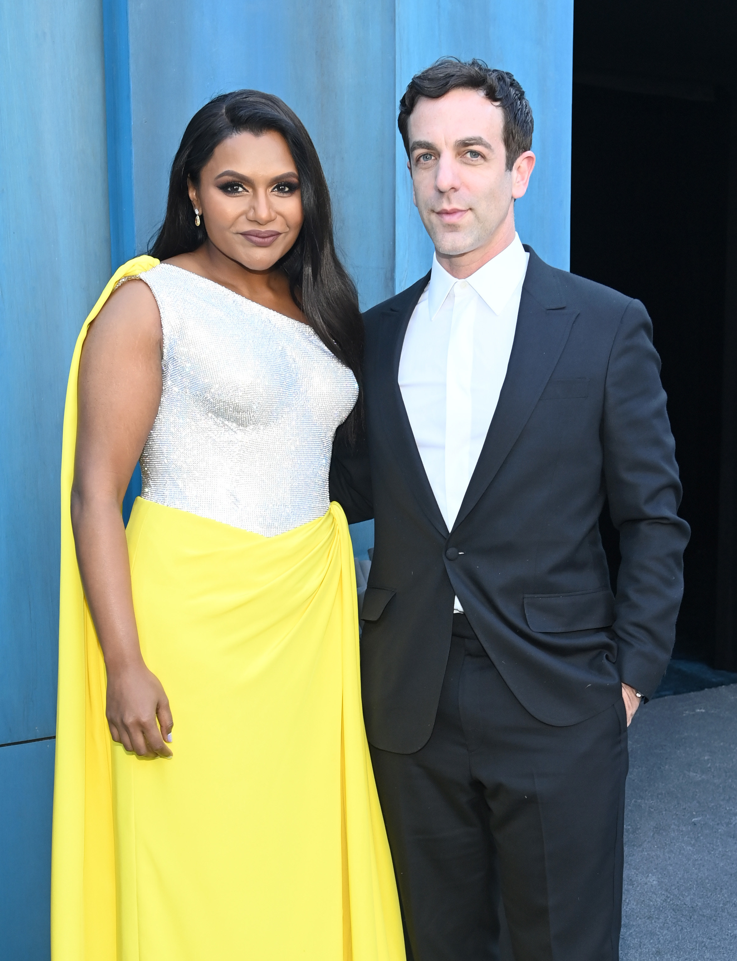 Mindy wearing a one-shoulder gown as she stands next to BJ