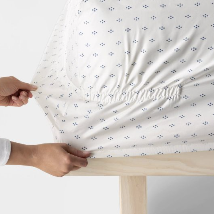 person tucking the sheet onto their mattress to show the full perimeter elastic that makes it stay secure