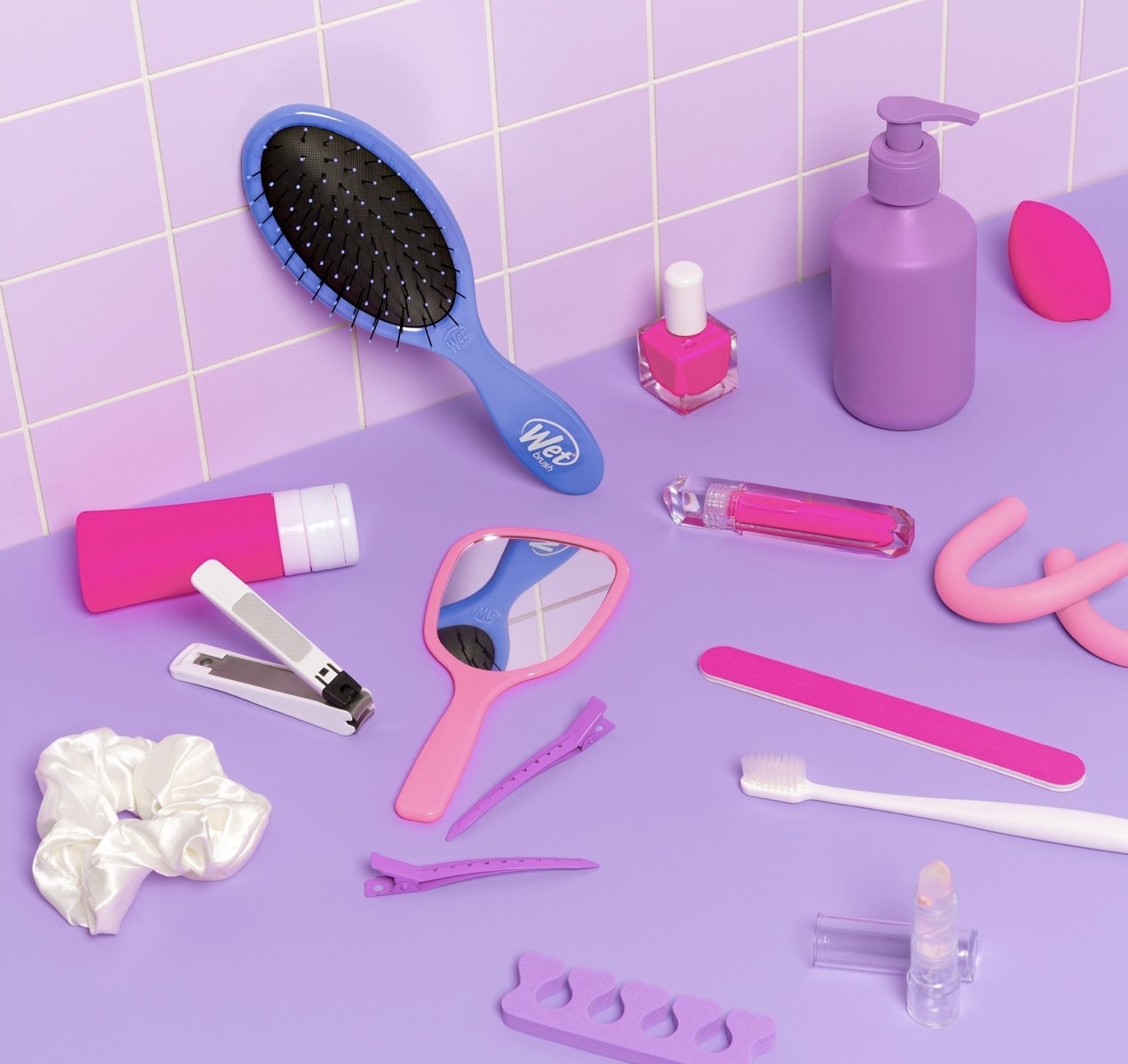 A purple hair brush, a mirror, nail file, nail clip, toothbrush, pink nail polish, a beauty blender, and a scrunchie