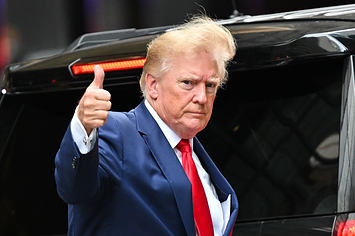 Trump gives a thumbs up as wind blows his hair as he steps into a car