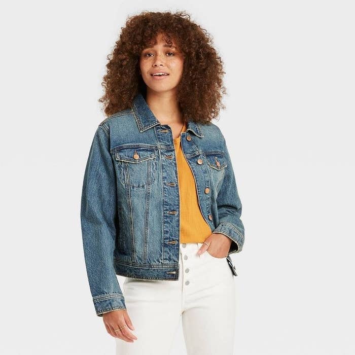 model wearing denim trucker jacket over a yellow top with white jeans