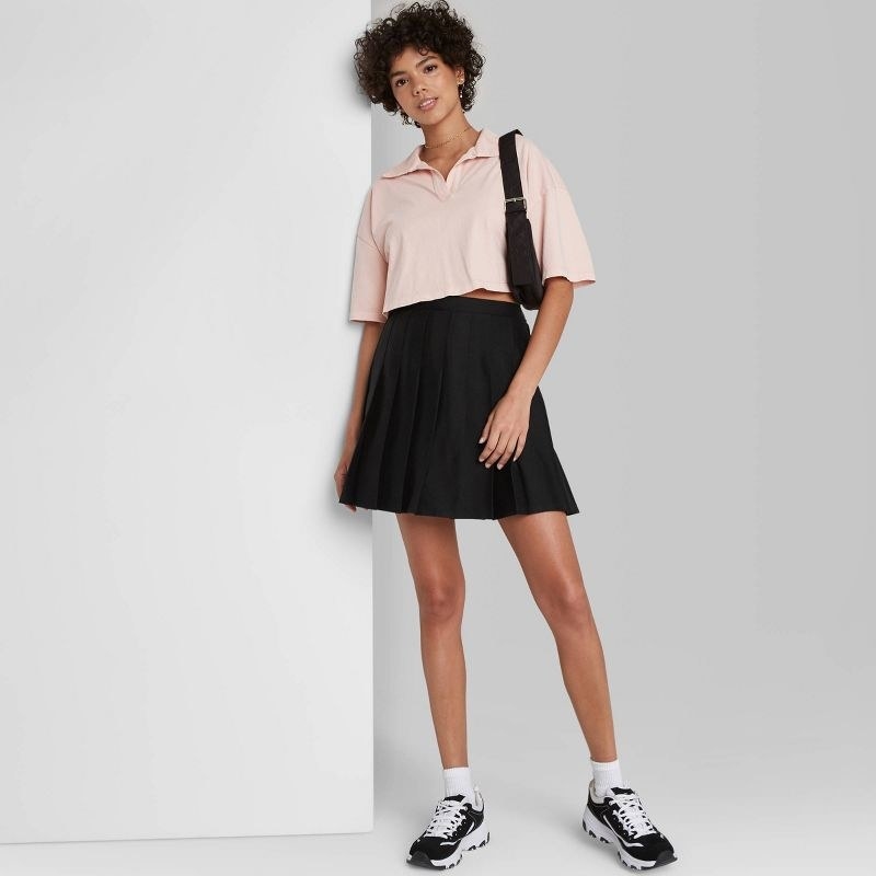 model wearing black pleated skirt with a pink crop top