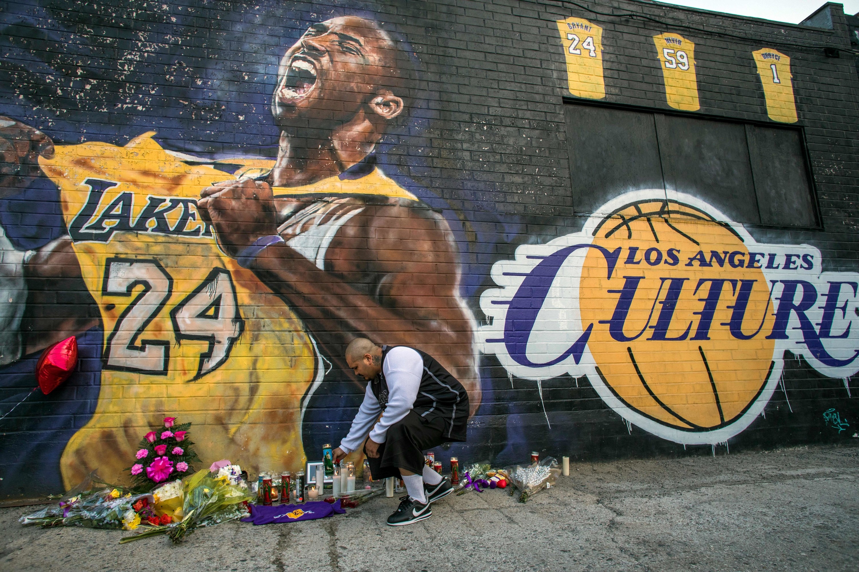 Luis Villanueva lights a candle in front of a Kobe Bryant mural in which he holds up his number 24 jersey beside the words &quot;los angeles culture&quot; written in the font of the Lakers basketball team