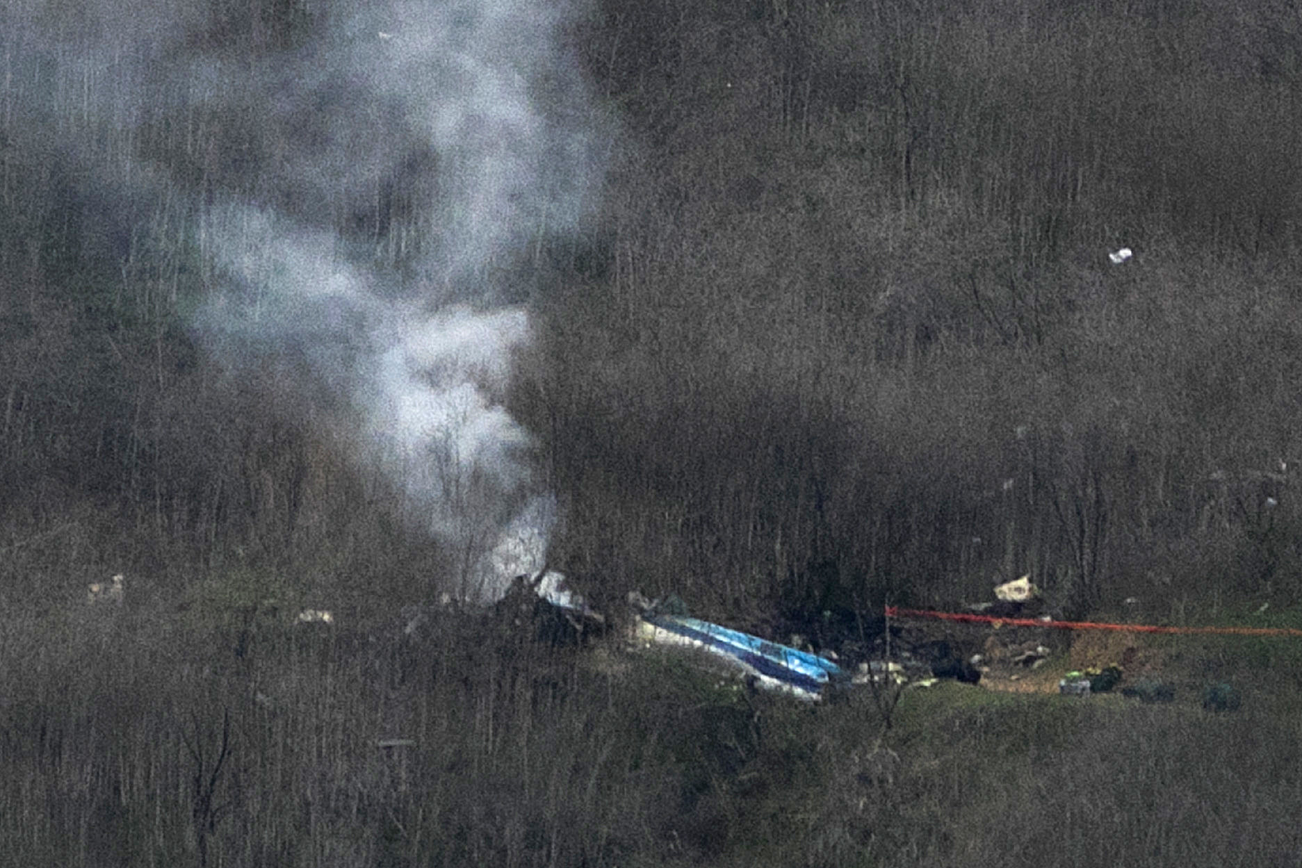 Smoldering, smoking wreckage of the crashed helicopter site in a wooded area