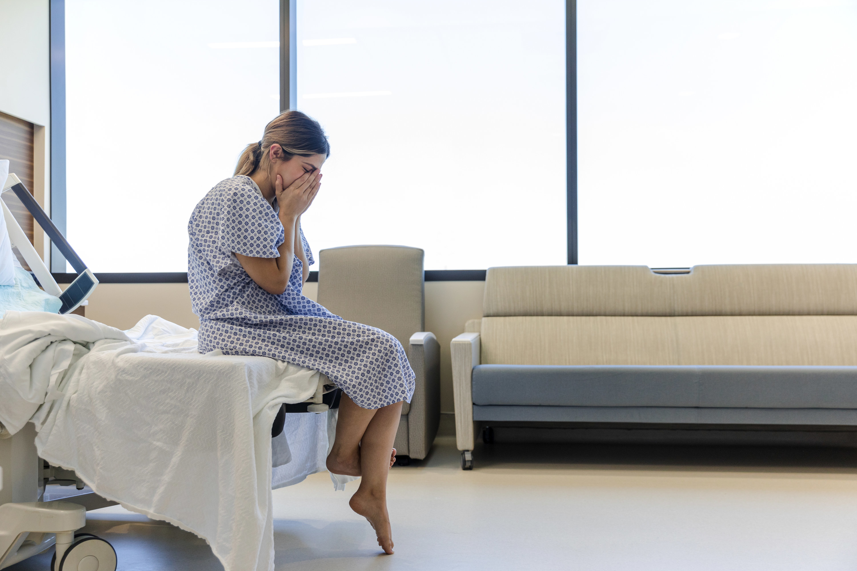 Woman sitting on the edge of a hospital bed with her face in her hands