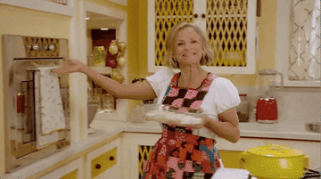 Amy Sedaris cooking and setting the over on fire, she turns around frazzled with smoke on her face