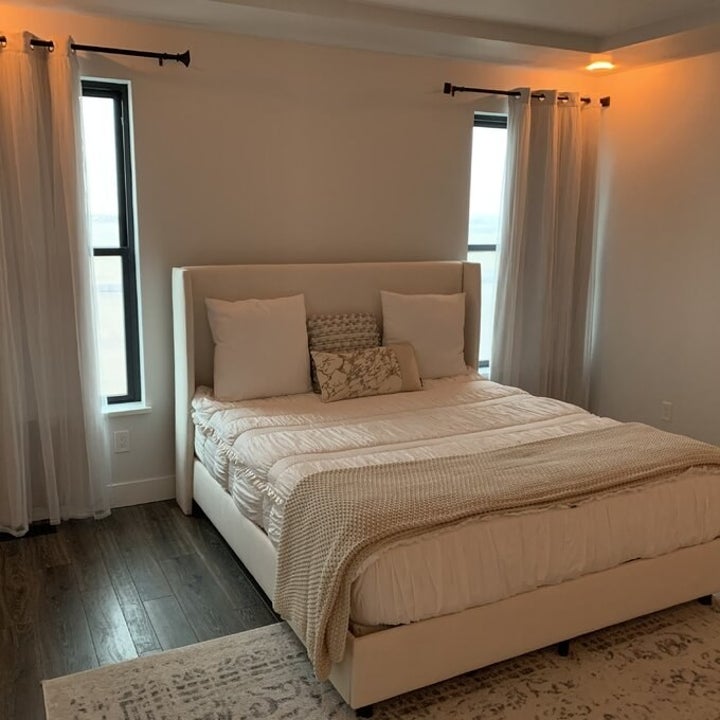 Beige curtains on windows on either side of bed