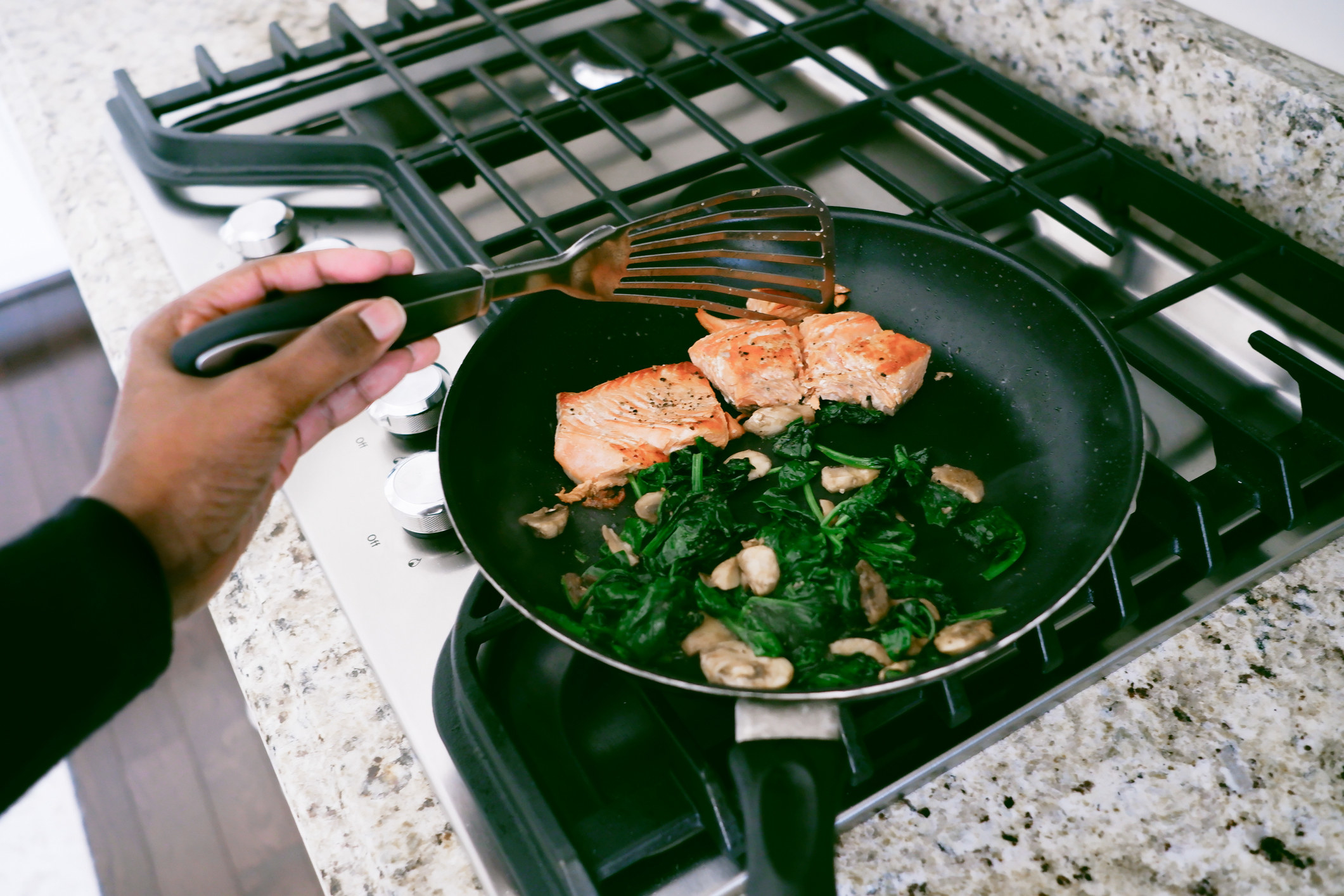Woman cooking salmon with spinach and mushrooms.