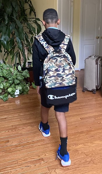 reviewer's photo of their child wearing the camo backpack