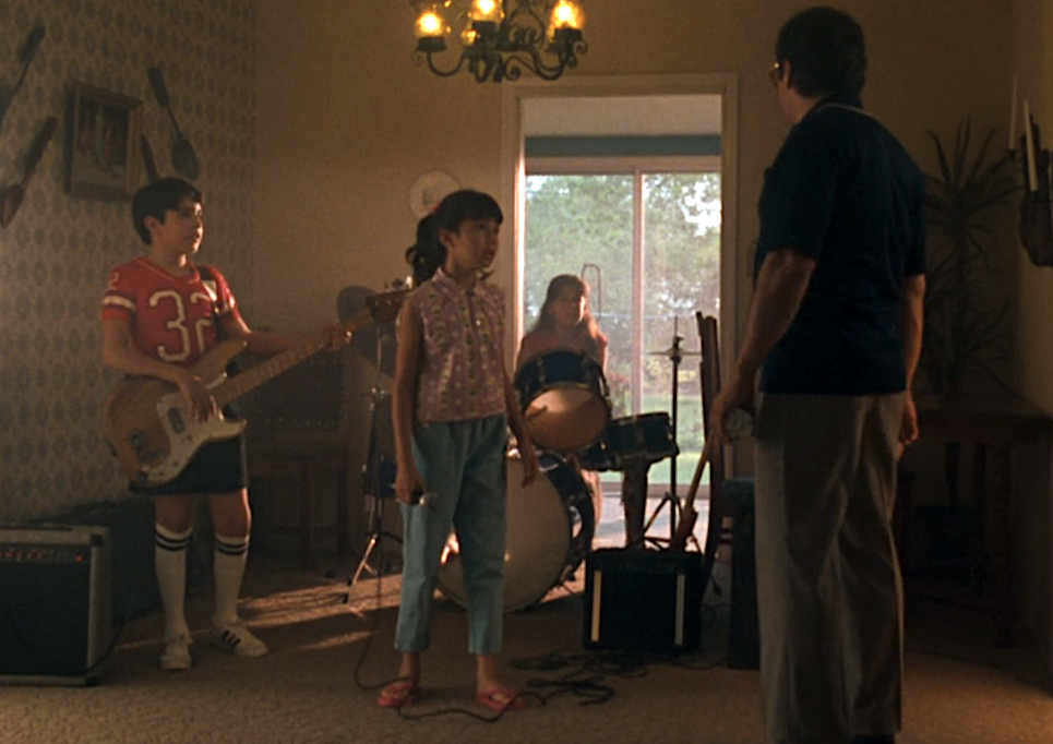 Three kids playing music and a man looking at them