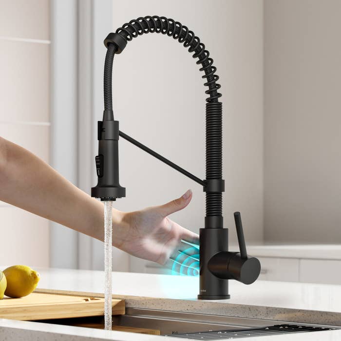a person waving their hand in front of the matte black faucet
