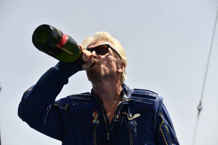 Richard Branson wears sunglasses and drinks from a bottle of champagne