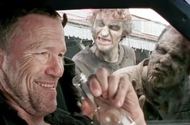 Merle Dixon sits in a car laughing surrounded by zombies
