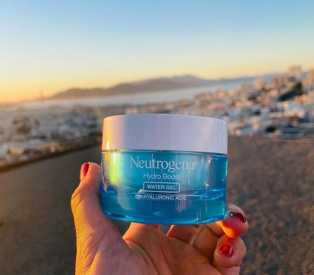 a hand holding the jar of Neutrogena hydro boost in front of the ocean