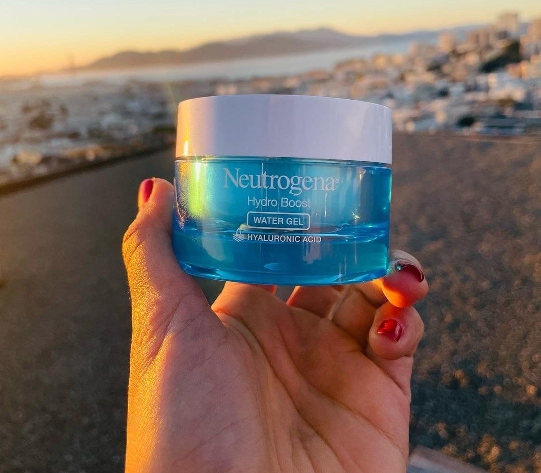 a hand holding the jar of Neutrogena hydro boost in front of the ocean